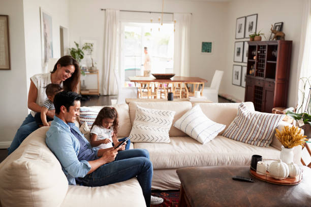 Young Hispanic Family Sitting On Sofa Reading A Book Together In Their  Living Room Stock Photo - Download Image Now - Istock